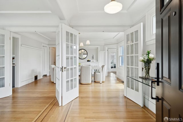 hallway with a decorative wall, ornamental molding, french doors, and light wood-type flooring