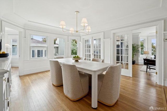 dining area featuring an inviting chandelier, ornamental molding, a decorative wall, and light wood-type flooring