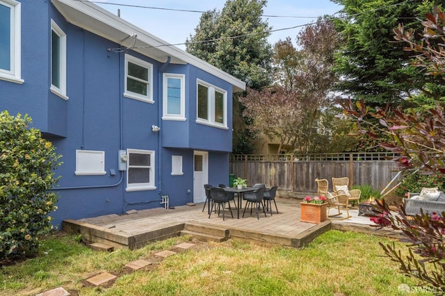 back of house with fence, a wooden deck, stucco siding, and a lawn
