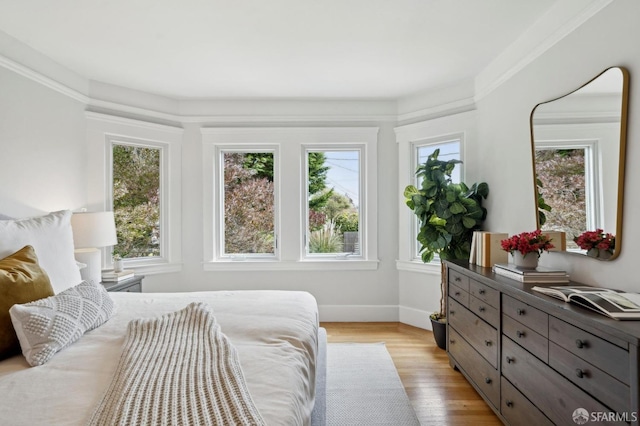 bedroom featuring light wood-style floors, baseboards, multiple windows, and ornamental molding