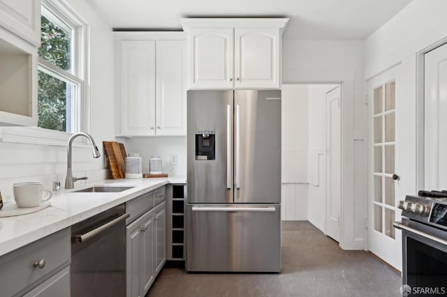kitchen featuring white cabinets, appliances with stainless steel finishes, light stone counters, a sink, and gray cabinets