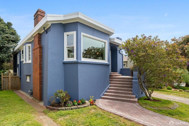 view of front of home featuring a front lawn, stucco siding, a chimney, and fence