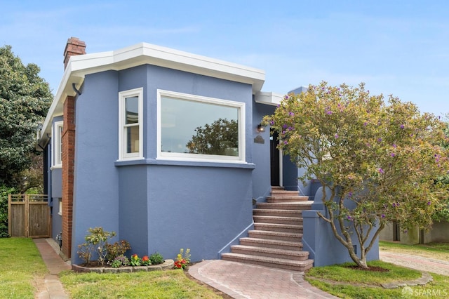 view of front of property with fence, stucco siding, and a chimney