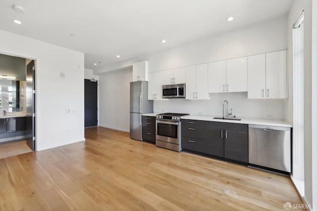 kitchen with light wood-type flooring, appliances with stainless steel finishes, sink, and white cabinets