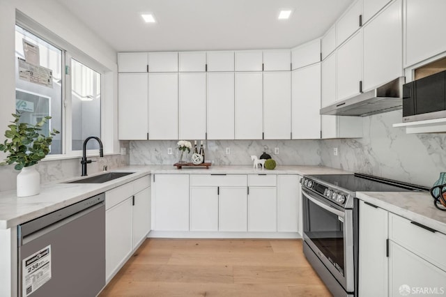 kitchen with under cabinet range hood, a sink, appliances with stainless steel finishes, light wood-type flooring, and decorative backsplash