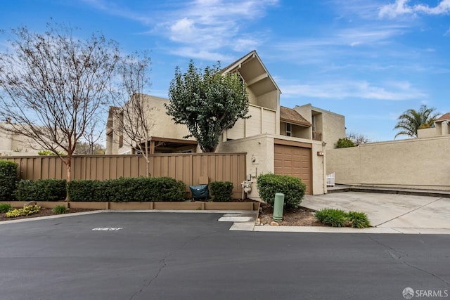 view of front facade with a garage, driveway, fence, and stucco siding