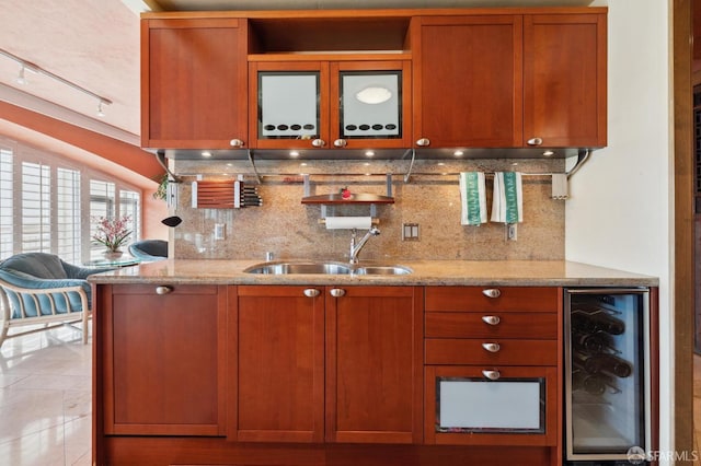 kitchen with light stone countertops, beverage cooler, brown cabinets, tasteful backsplash, and a sink