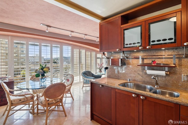 kitchen featuring a sink, light stone counters, decorative backsplash, and brown cabinetry