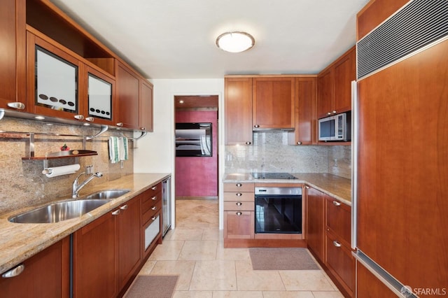 kitchen featuring brown cabinets, light stone countertops, a sink, tasteful backsplash, and black appliances