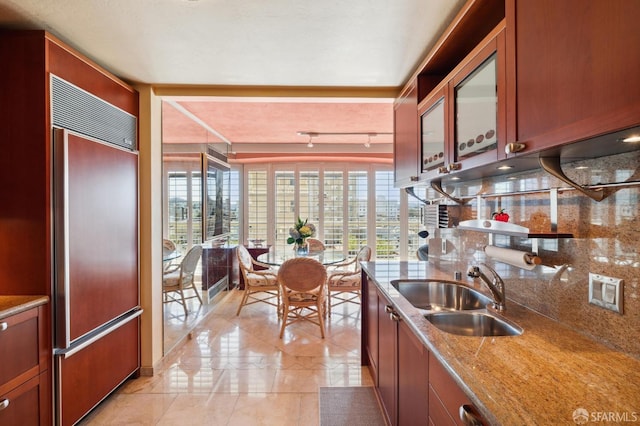 kitchen with paneled refrigerator, stone counters, a sink, and tasteful backsplash