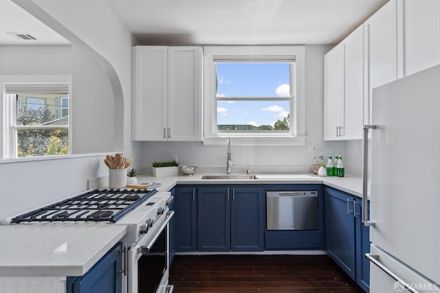 kitchen with appliances with stainless steel finishes, blue cabinets, sink, white cabinets, and dark hardwood / wood-style flooring