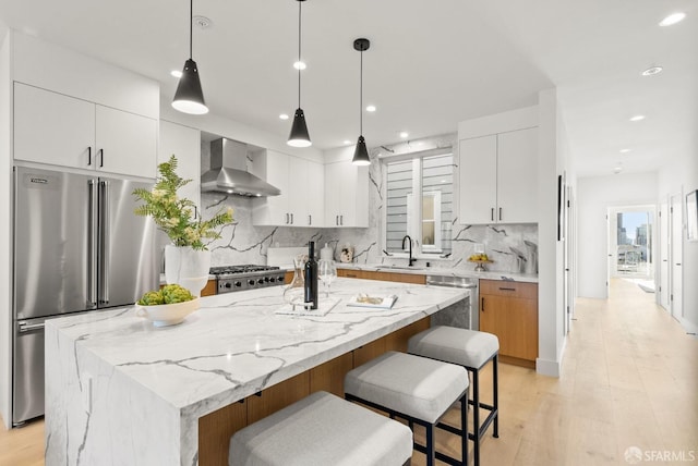 kitchen featuring hanging light fixtures, white cabinets, wall chimney range hood, and a center island