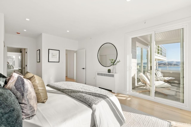 bedroom featuring radiator, light hardwood / wood-style floors, and a water view