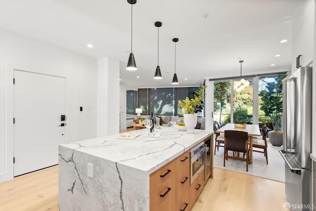 kitchen with white cabinets, stainless steel appliances, hanging light fixtures, light stone counters, and expansive windows