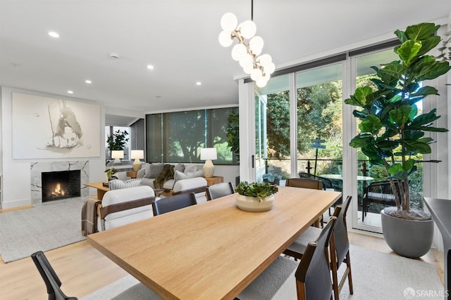 dining space featuring a premium fireplace, light hardwood / wood-style floors, expansive windows, and a notable chandelier