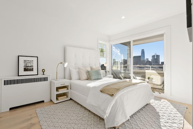 bedroom with light hardwood / wood-style floors, access to exterior, and radiator heating unit