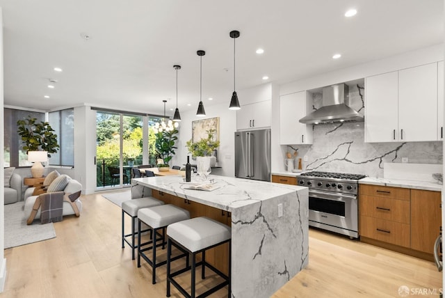 kitchen with white cabinetry, light stone countertops, an island with sink, wall chimney exhaust hood, and high quality appliances