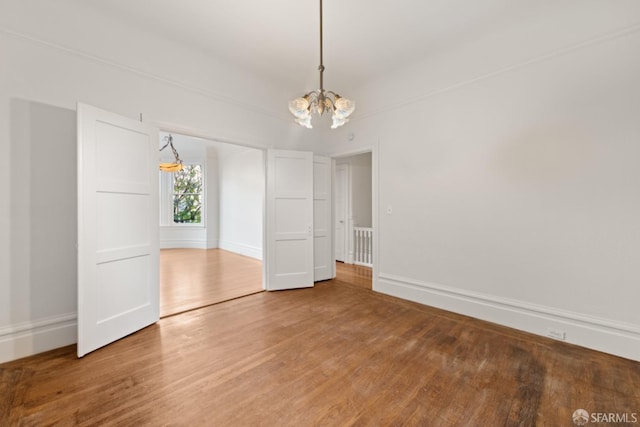 spare room with wood-type flooring and an inviting chandelier