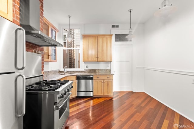 kitchen featuring wall chimney exhaust hood, light brown cabinetry, sink, appliances with stainless steel finishes, and pendant lighting