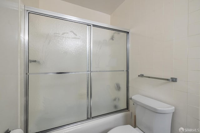 bathroom with toilet, shower / bath combination with glass door, and tile walls