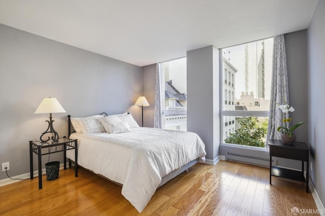 bedroom with a baseboard heating unit and wood-type flooring