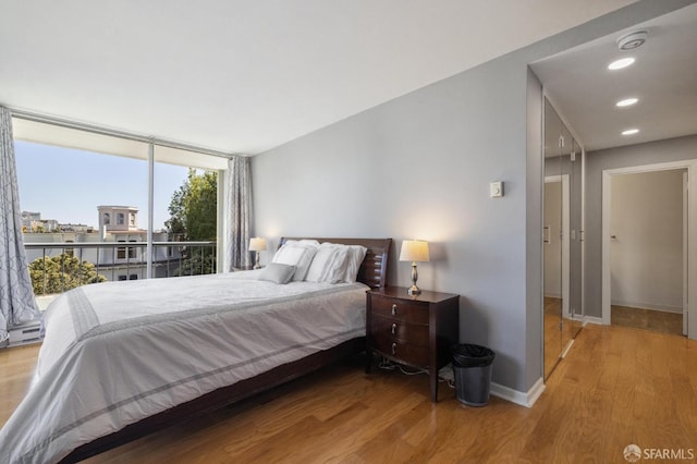 bedroom with expansive windows, wood-type flooring, and baseboard heating