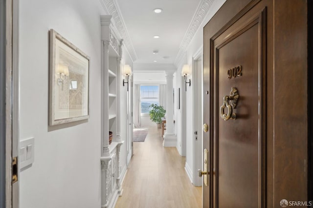 hallway with crown molding, light wood-type flooring, built in features, and ornate columns