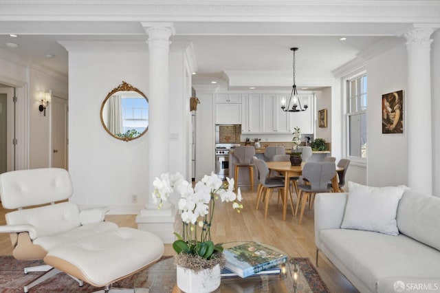 living room featuring light hardwood / wood-style flooring, a notable chandelier, ornamental molding, and decorative columns