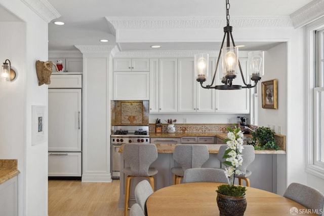 kitchen featuring decorative light fixtures, white cabinets, high end appliances, ornamental molding, and light stone countertops