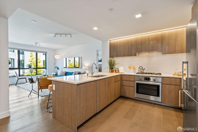 kitchen featuring light wood-style flooring, a peninsula, a sink, open floor plan, and appliances with stainless steel finishes