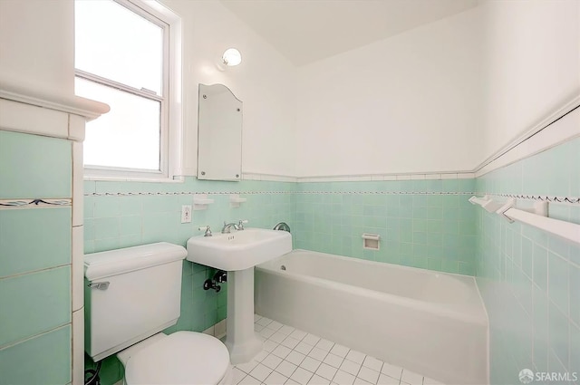 full bathroom featuring wainscoting, toilet, tile patterned floors, a washtub, and tile walls