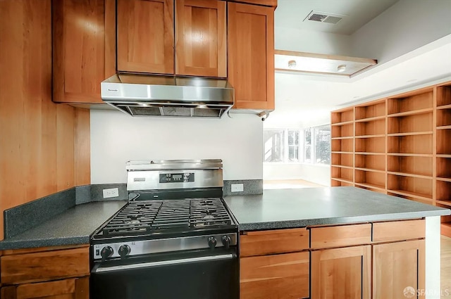 kitchen featuring dark countertops, visible vents, brown cabinetry, stainless steel gas range oven, and extractor fan