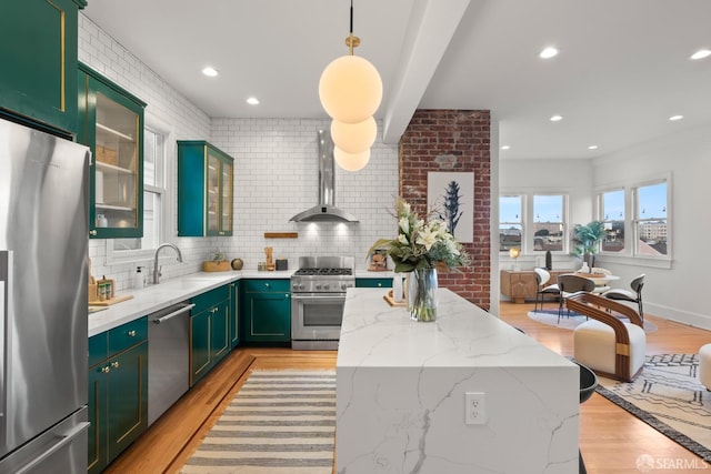 kitchen with light stone countertops, appliances with stainless steel finishes, sink, and wall chimney exhaust hood