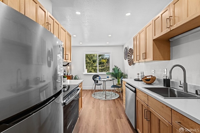 kitchen with light brown cabinetry, sink, stainless steel appliances, a textured ceiling, and light hardwood / wood-style flooring