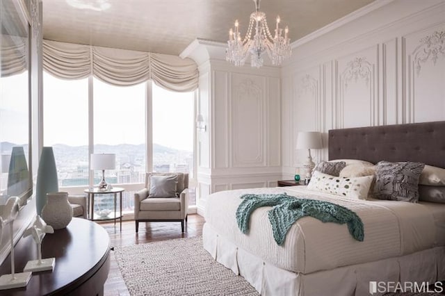 bedroom with a decorative wall, ornamental molding, a mountain view, wood finished floors, and a notable chandelier