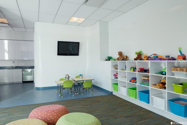 recreation room with a drop ceiling, sink, and concrete floors