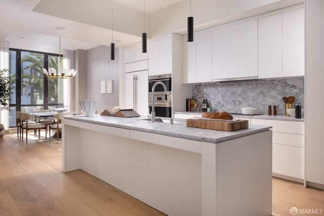 kitchen featuring white cabinetry, a kitchen island with sink, light hardwood / wood-style flooring, and pendant lighting