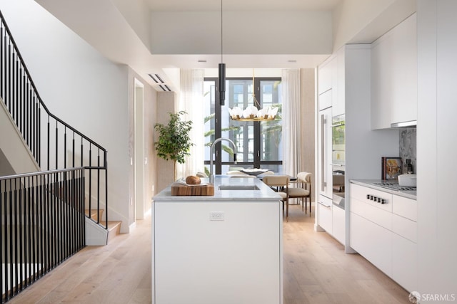 kitchen featuring an inviting chandelier, sink, light wood-type flooring, a kitchen island, and white cabinetry