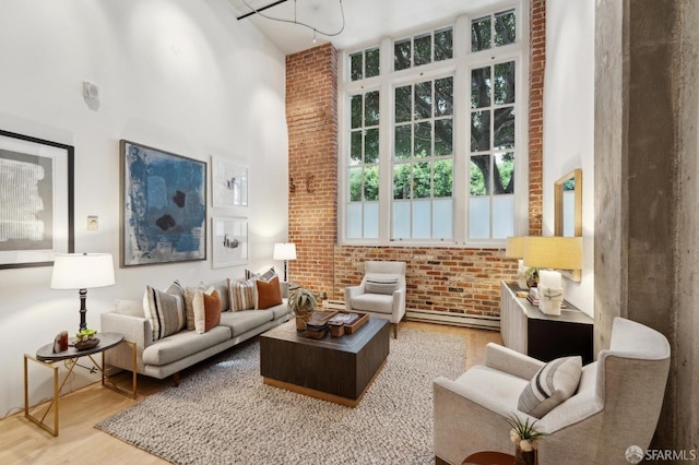 sitting room with a towering ceiling, brick wall, and wood finished floors