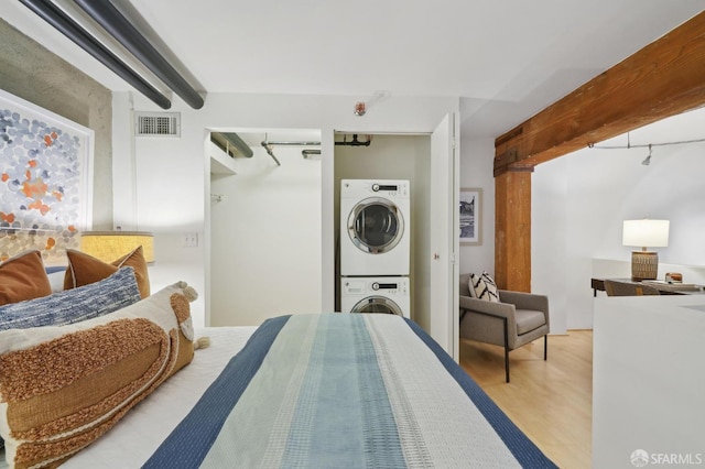 bedroom featuring visible vents, beam ceiling, wood finished floors, and stacked washer and clothes dryer