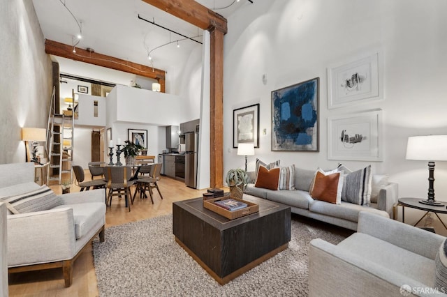 living area with light wood-style floors, rail lighting, beamed ceiling, and a high ceiling