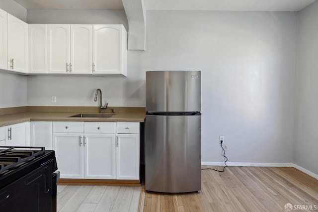 kitchen featuring sink, white cabinetry, light hardwood / wood-style flooring, and stainless steel refrigerator