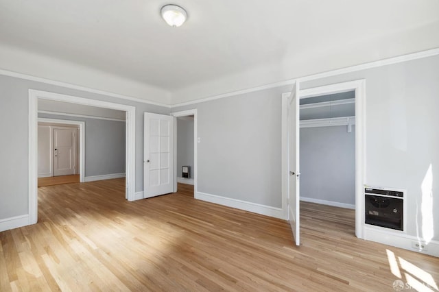 unfurnished bedroom featuring a closet, ornamental molding, heating unit, and light wood-type flooring