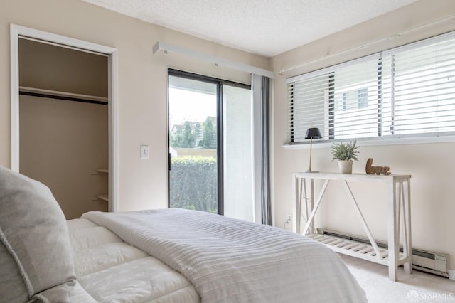 carpeted bedroom with a textured ceiling, a spacious closet, a baseboard heating unit, and a closet