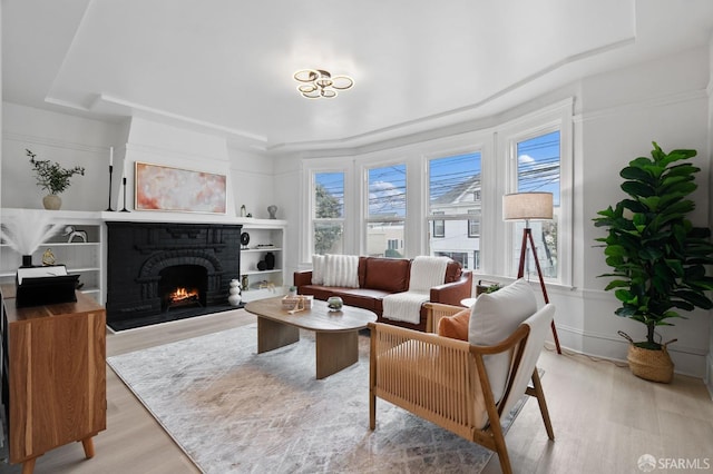 living room featuring light wood-style flooring, a fireplace, and a raised ceiling