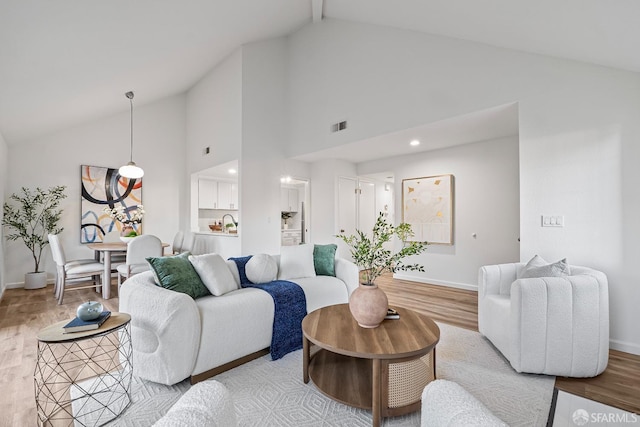 living area with high vaulted ceiling, baseboards, visible vents, and light wood finished floors