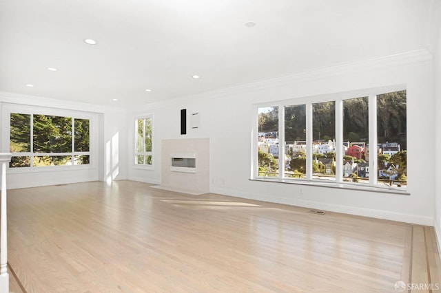 unfurnished living room with a healthy amount of sunlight, ornamental molding, and light hardwood / wood-style flooring