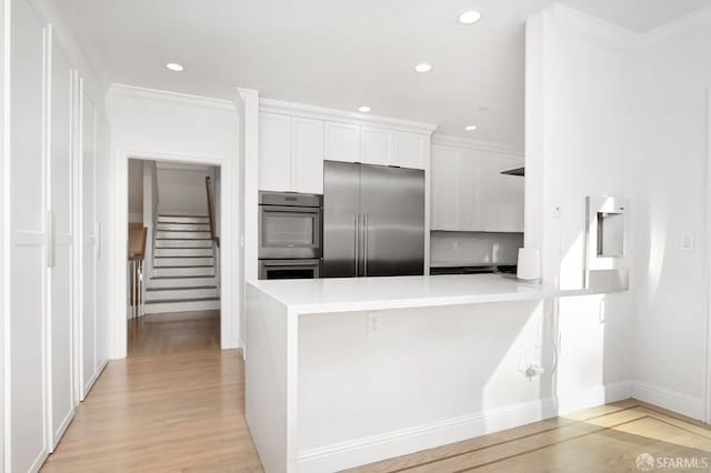 kitchen with kitchen peninsula, ornamental molding, appliances with stainless steel finishes, light hardwood / wood-style floors, and white cabinetry