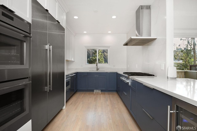 kitchen with sink, stainless steel appliances, light hardwood / wood-style flooring, range hood, and white cabinets