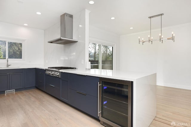 kitchen with kitchen peninsula, wall chimney exhaust hood, beverage cooler, and stainless steel gas cooktop